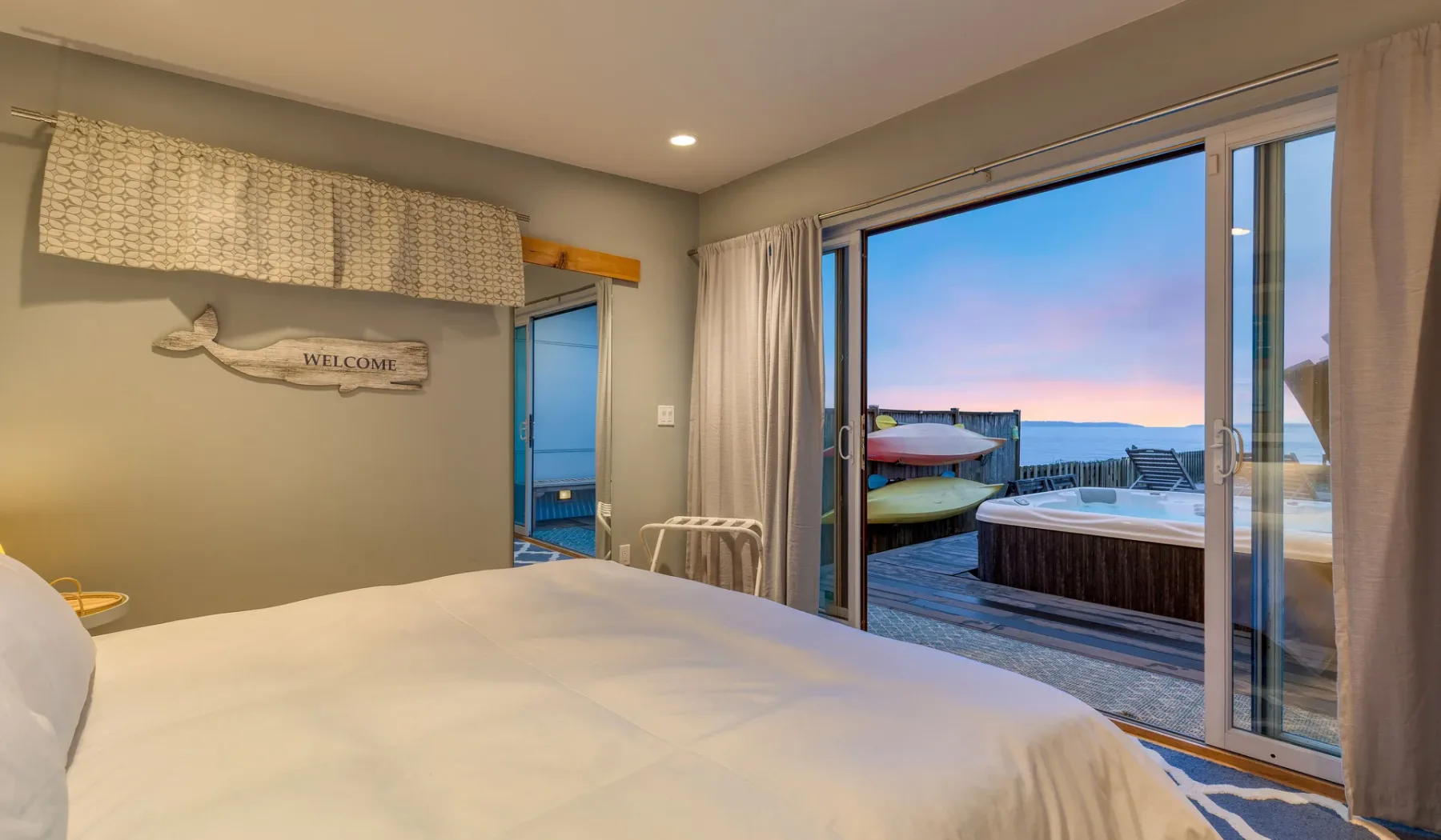 A bedroom opens onto a deck with a hot tub and ocean view.