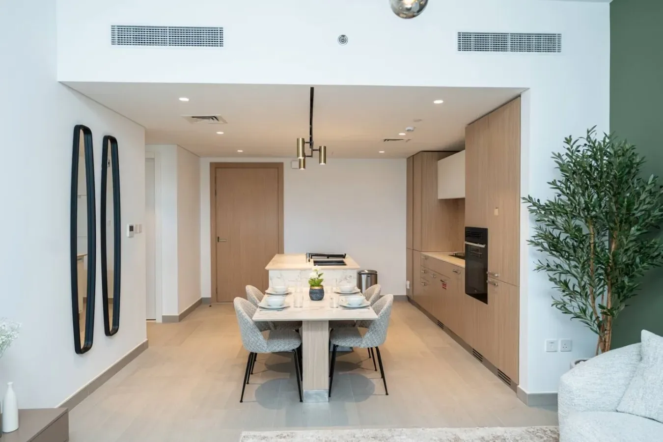 A modern dining area opens onto a kitchen, with a table set beneath pendant lights.