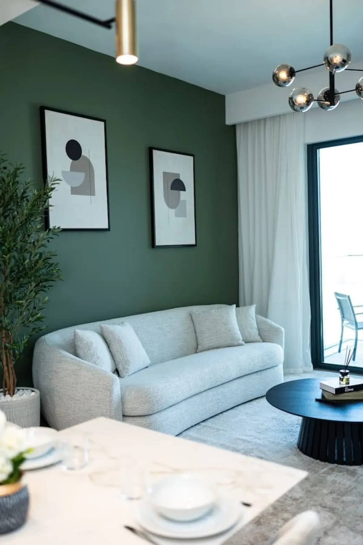 Living room with light seating, framed artwork, and a dark green wall.