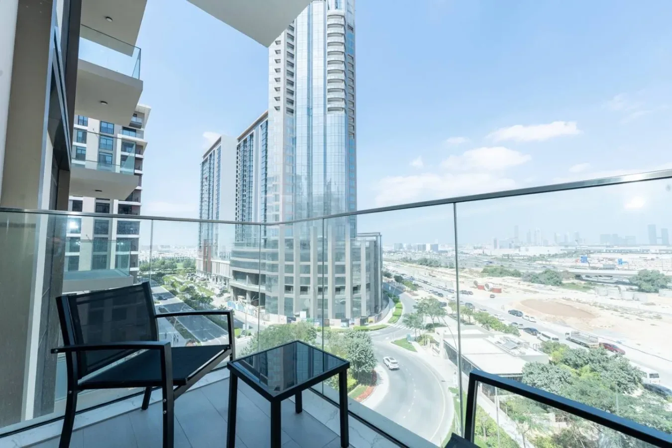 A balcony overlooks a city skyline, with outdoor seating beside the glass railing.