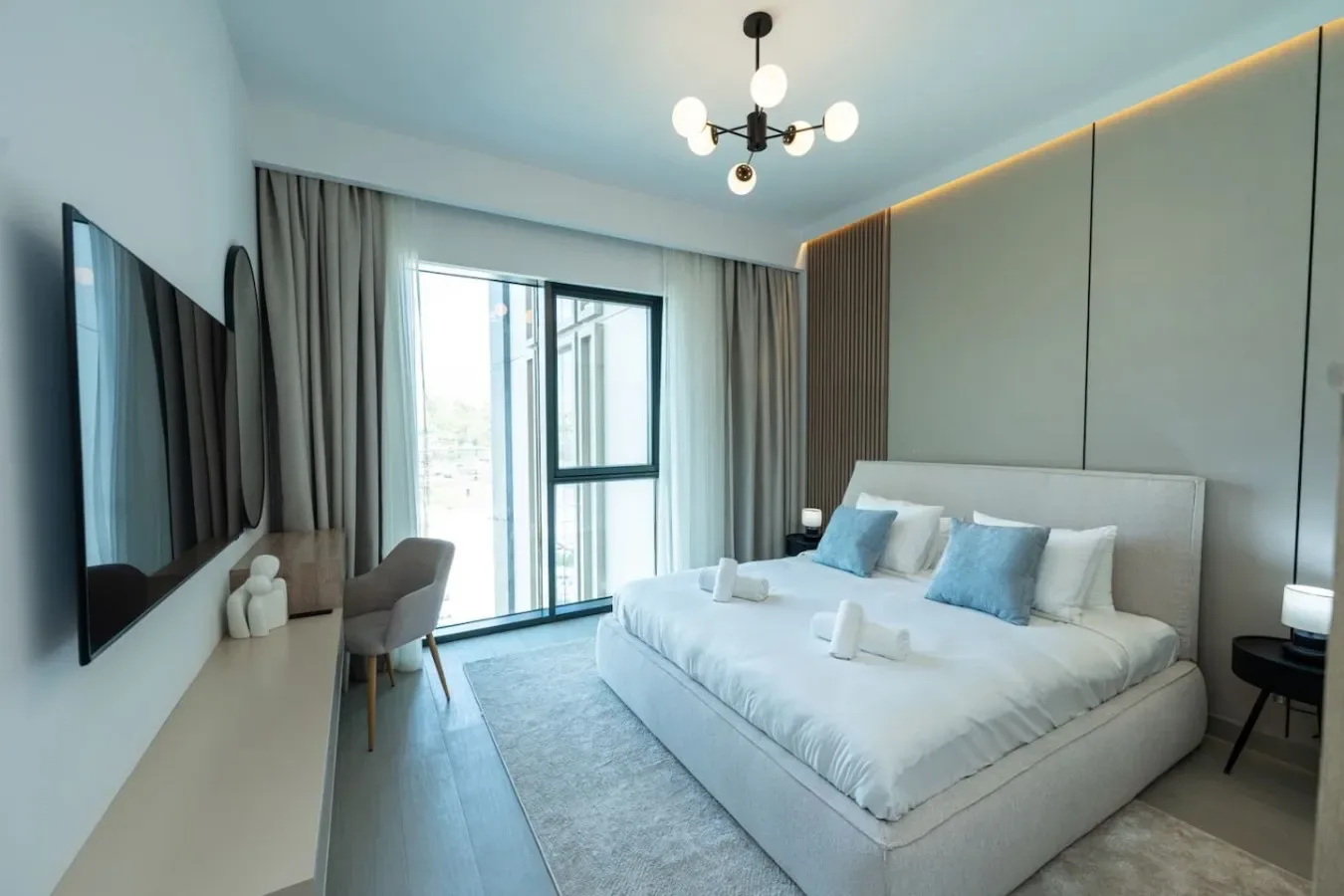 A bright bedroom with a large bed, blue pillows, and a wall-mounted television.