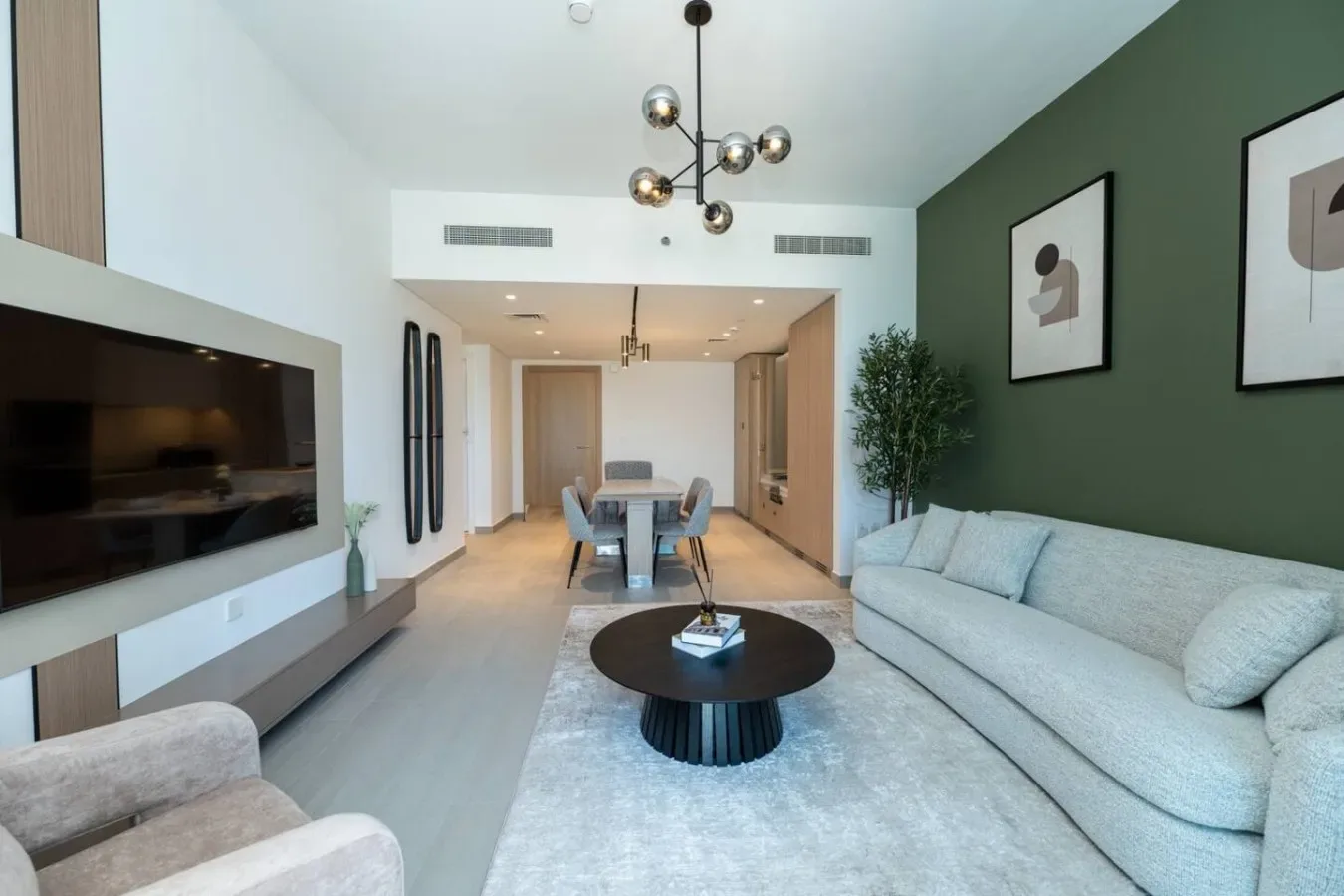 A modern living room with pale seating, a coffee table, and a dining area beyond.