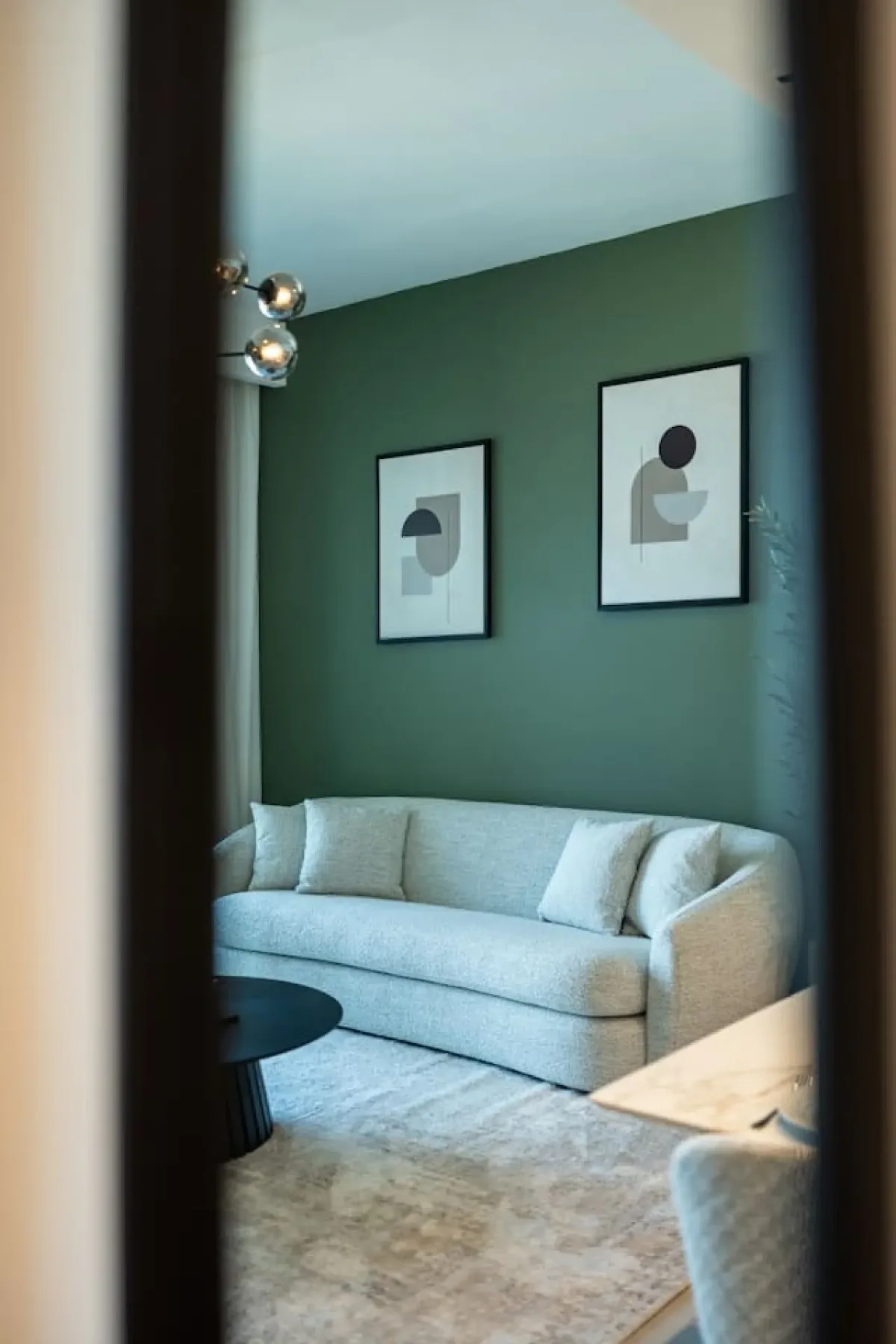 A living room with a light-colored sofa and framed abstract art on a green wall.