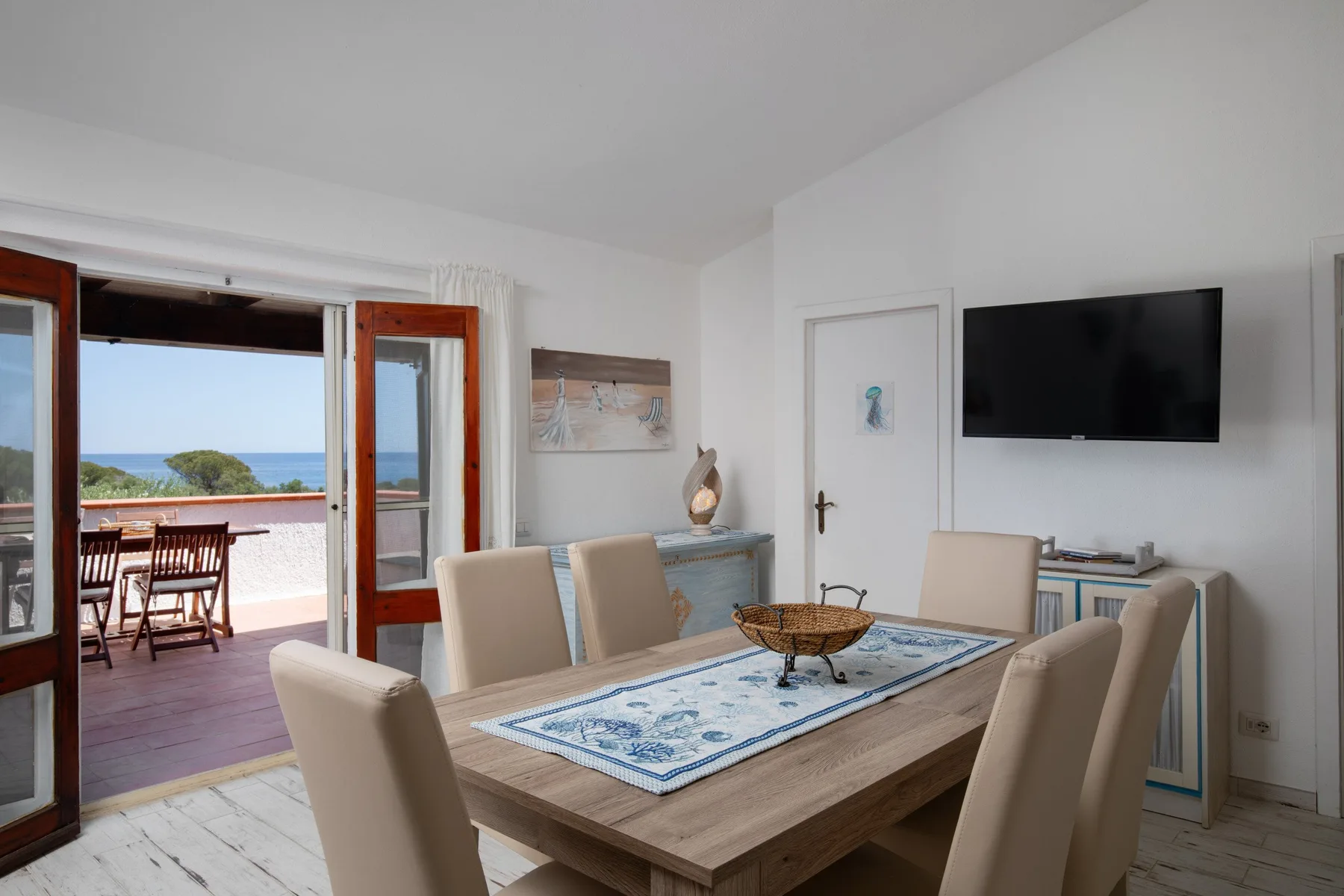 A dining area with a rectangular table and chairs beside open doors to a terrace.
