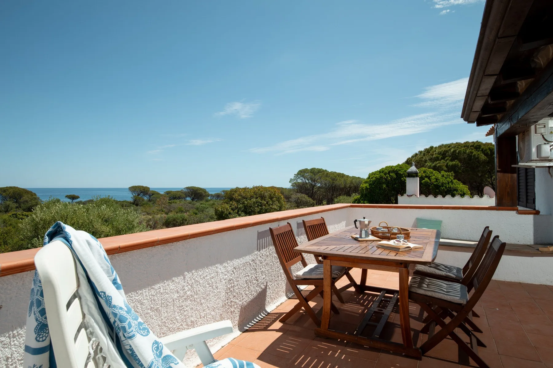 A sunny outdoor terrace with a wooden dining table and coastal views.