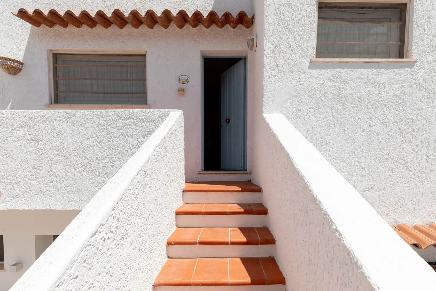 An exterior stairway leads to an open doorway beside shuttered windows.