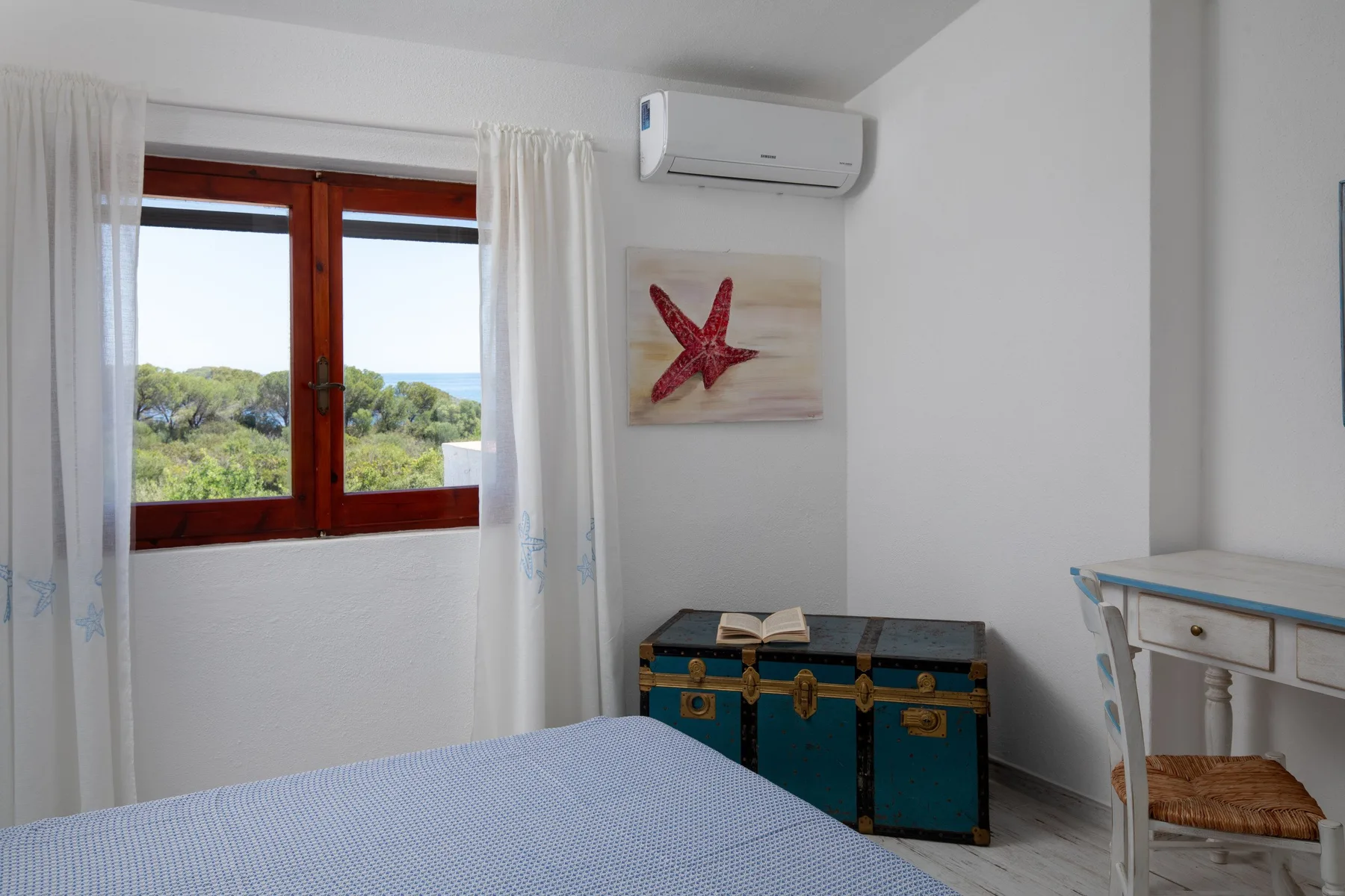 A bedroom with a bed beside a window overlooking greenery.