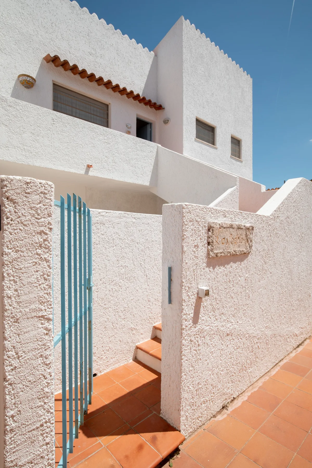 A white stucco building entrance opens onto terracotta-tiled steps.