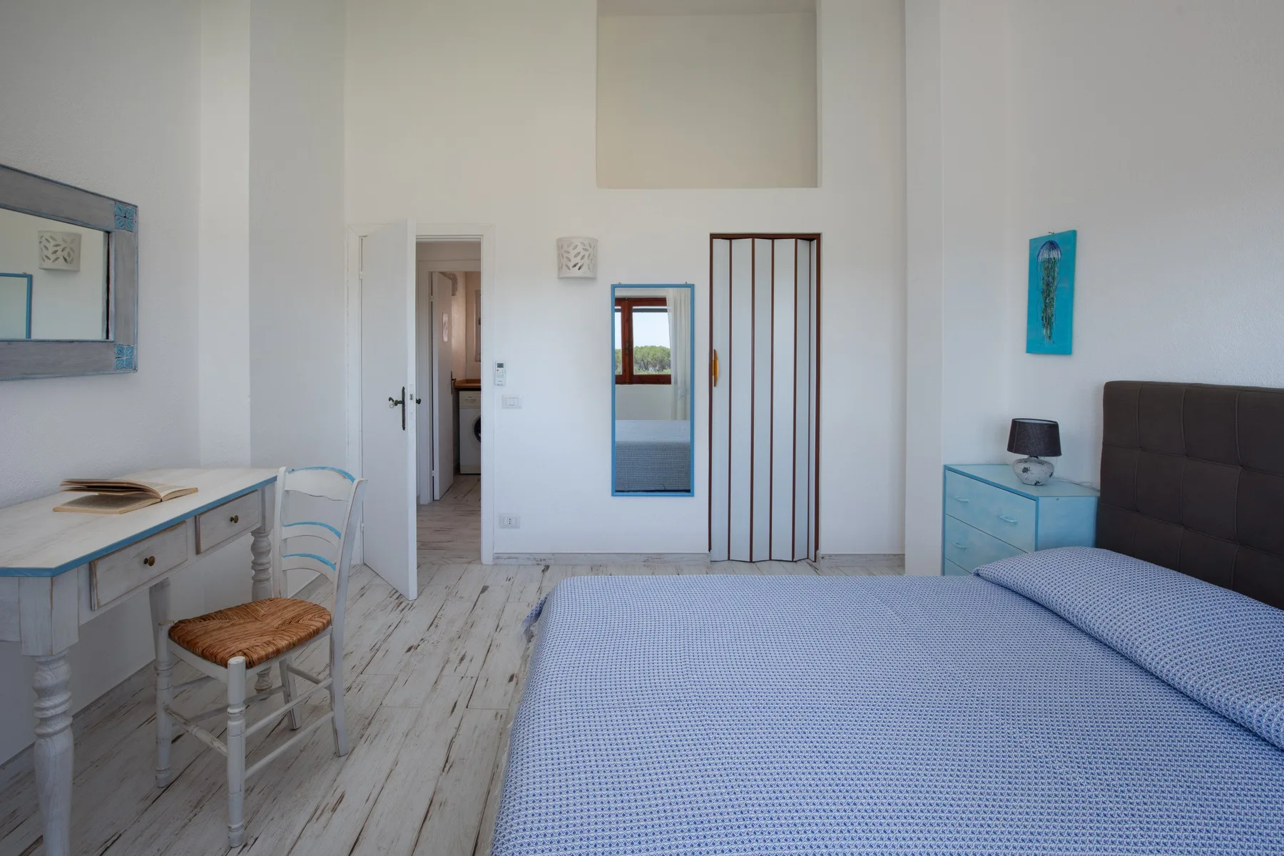 A bright bedroom with a bed, desk, and open doorway.