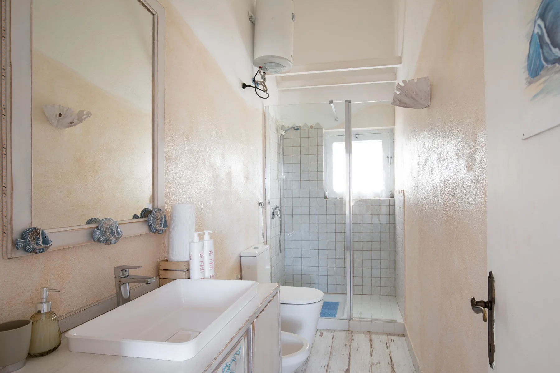 A narrow bathroom with a sink, toilet, and glass shower area.