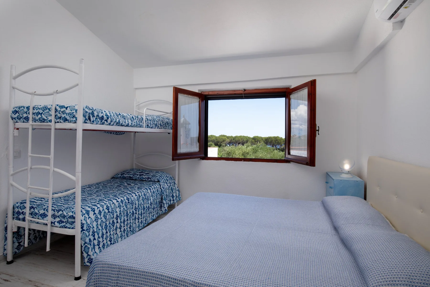 A bedroom with a double bed, bunk beds, and an open window overlooking greenery.