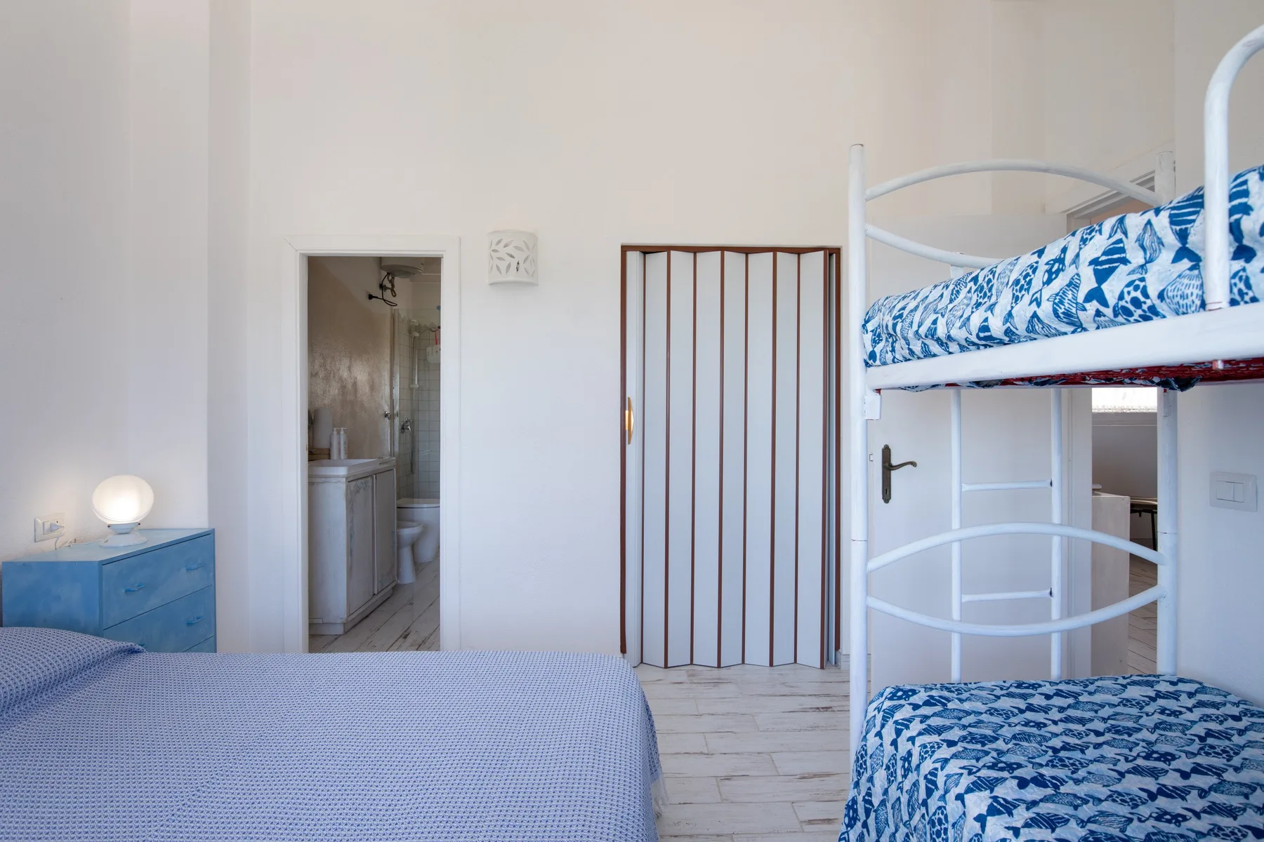 A bedroom with a bed, a blue bedside cabinet, and bunk beds.