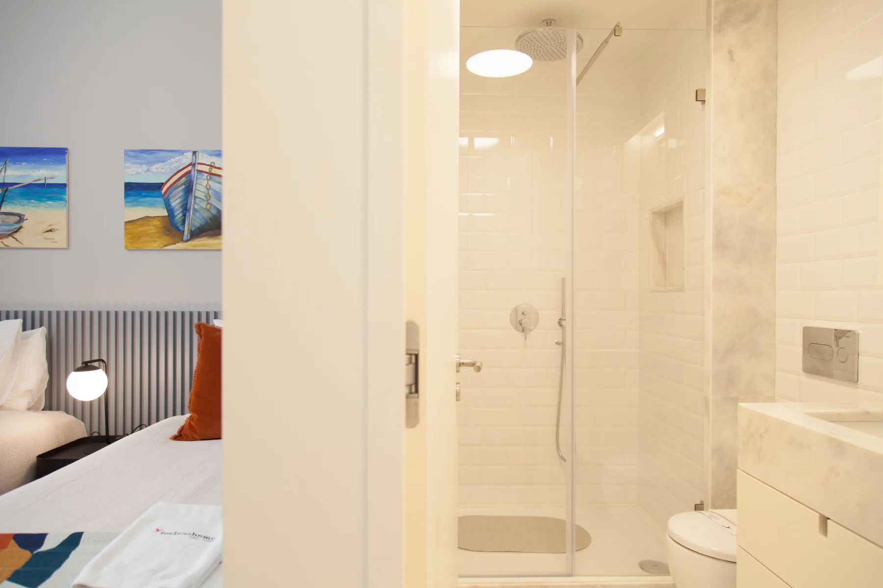A bedroom and adjoining bathroom with a glass shower and wall art.