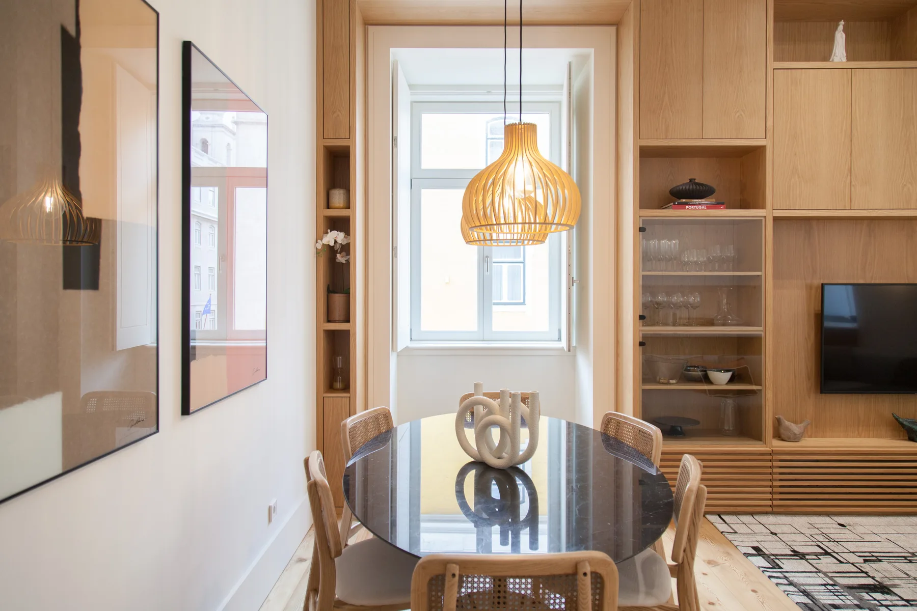 Dining area with a glass table, wooden seating, and built-in shelving.