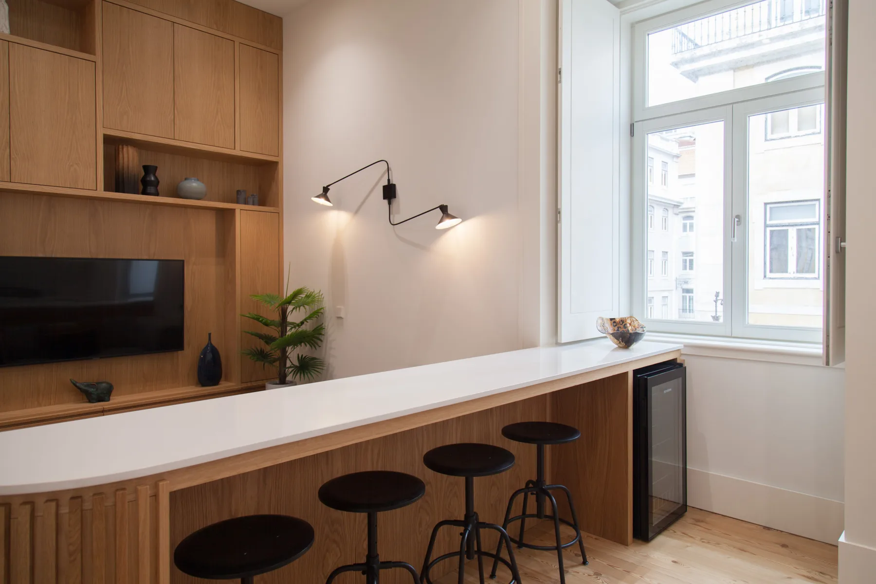 A bright living area features a wall-mounted television, counter, and seating by the window.