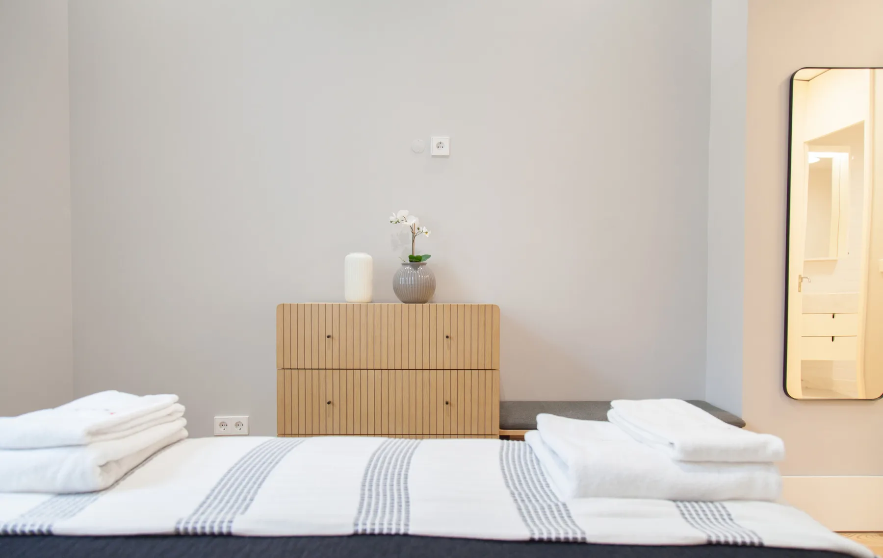 A bedroom with a low wooden dresser and neatly made bed.