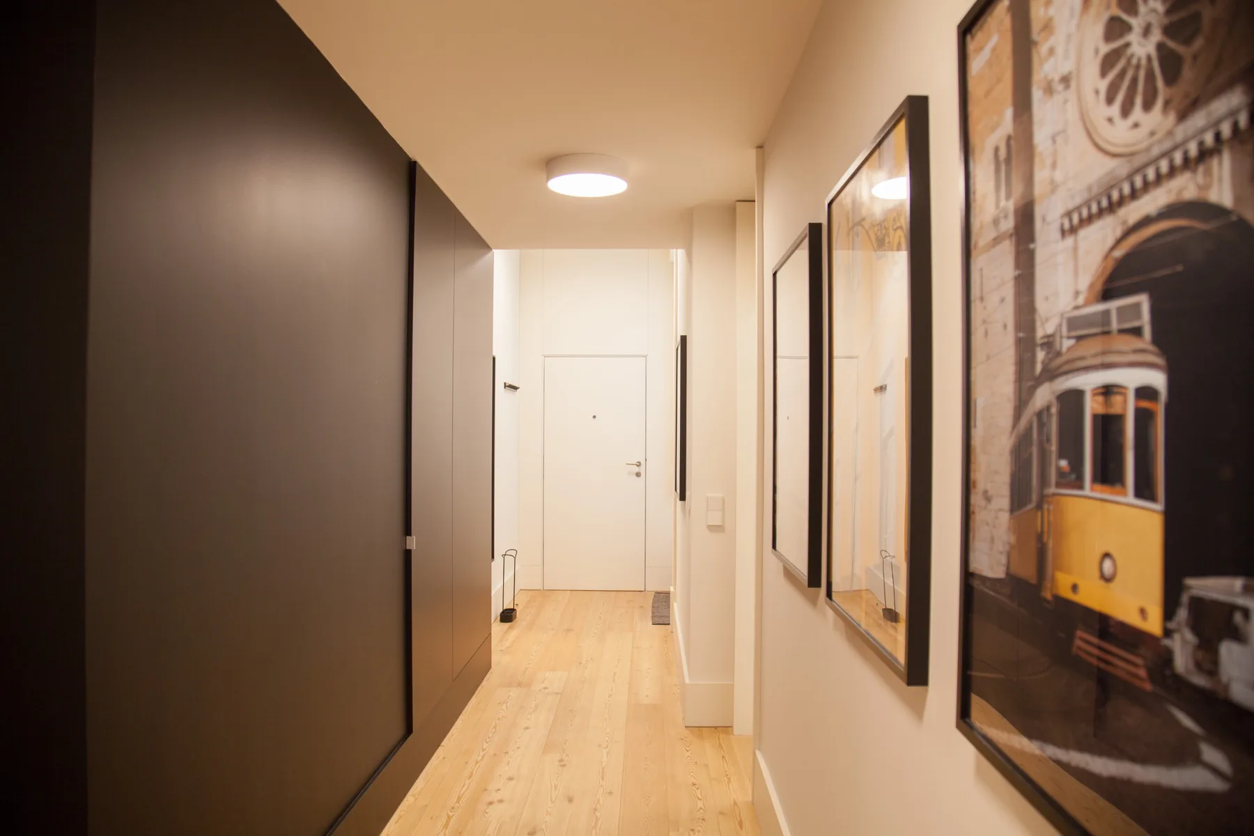 A bright hallway with light wood flooring and framed wall art.