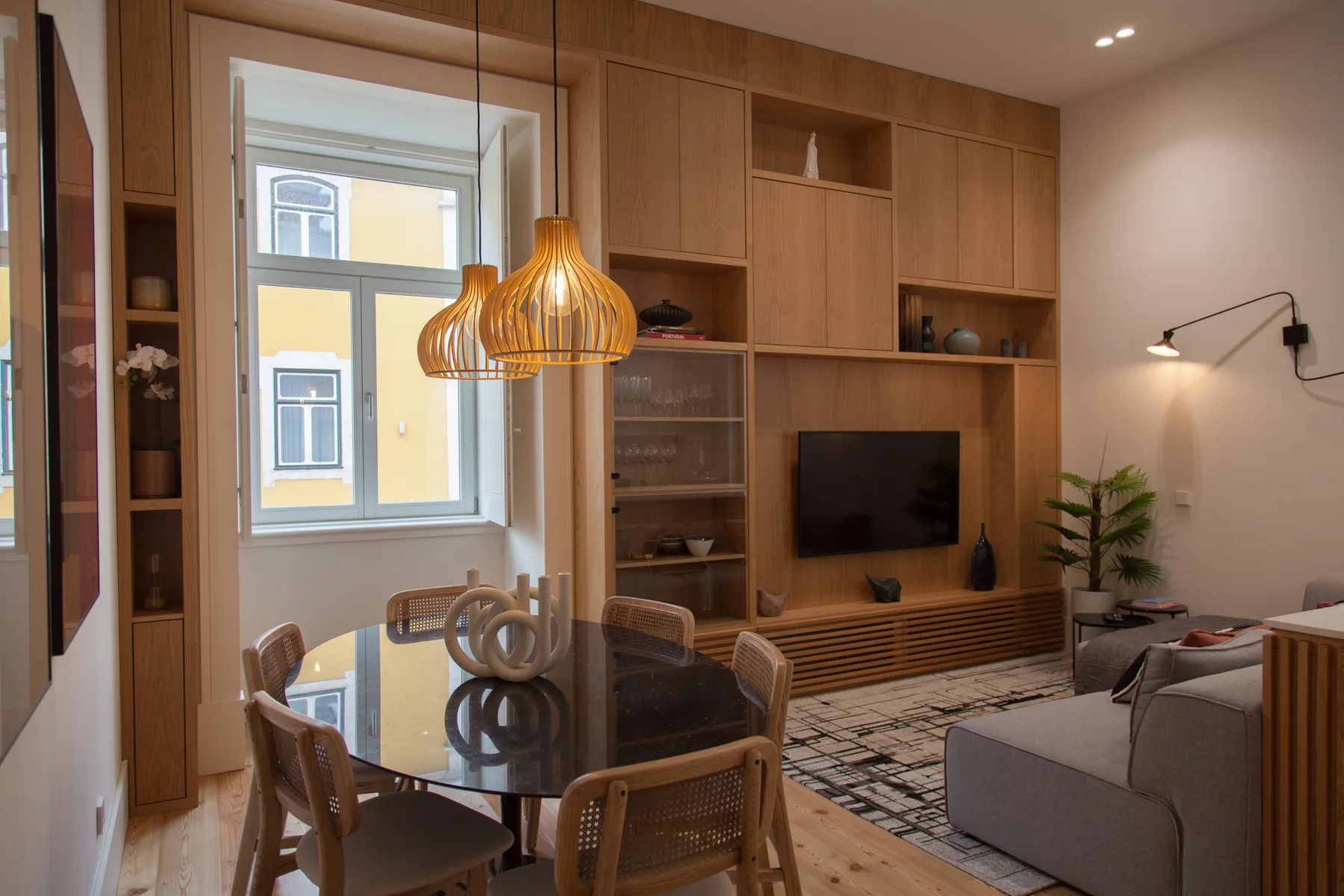 A living and dining area with wooden cabinetry, a television, and a glass dining table.