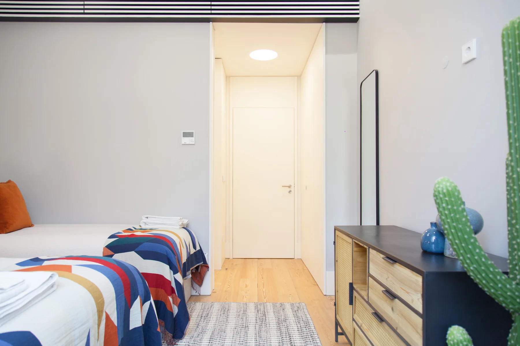 A bright bedroom with two beds, colorful bedding, and a dresser.