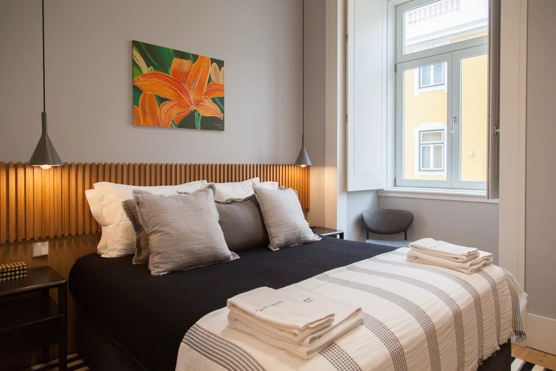 A bedroom with dark bedding, striped blankets, and colorful floral artwork.