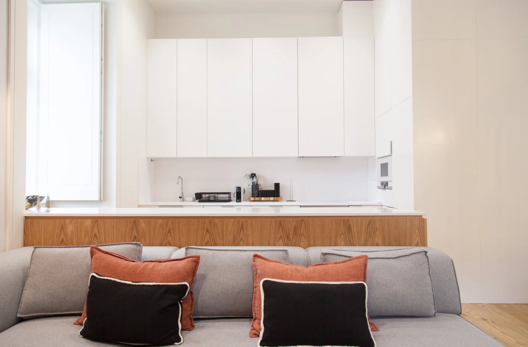 A bright open-plan living area with a compact kitchen behind the sofa.