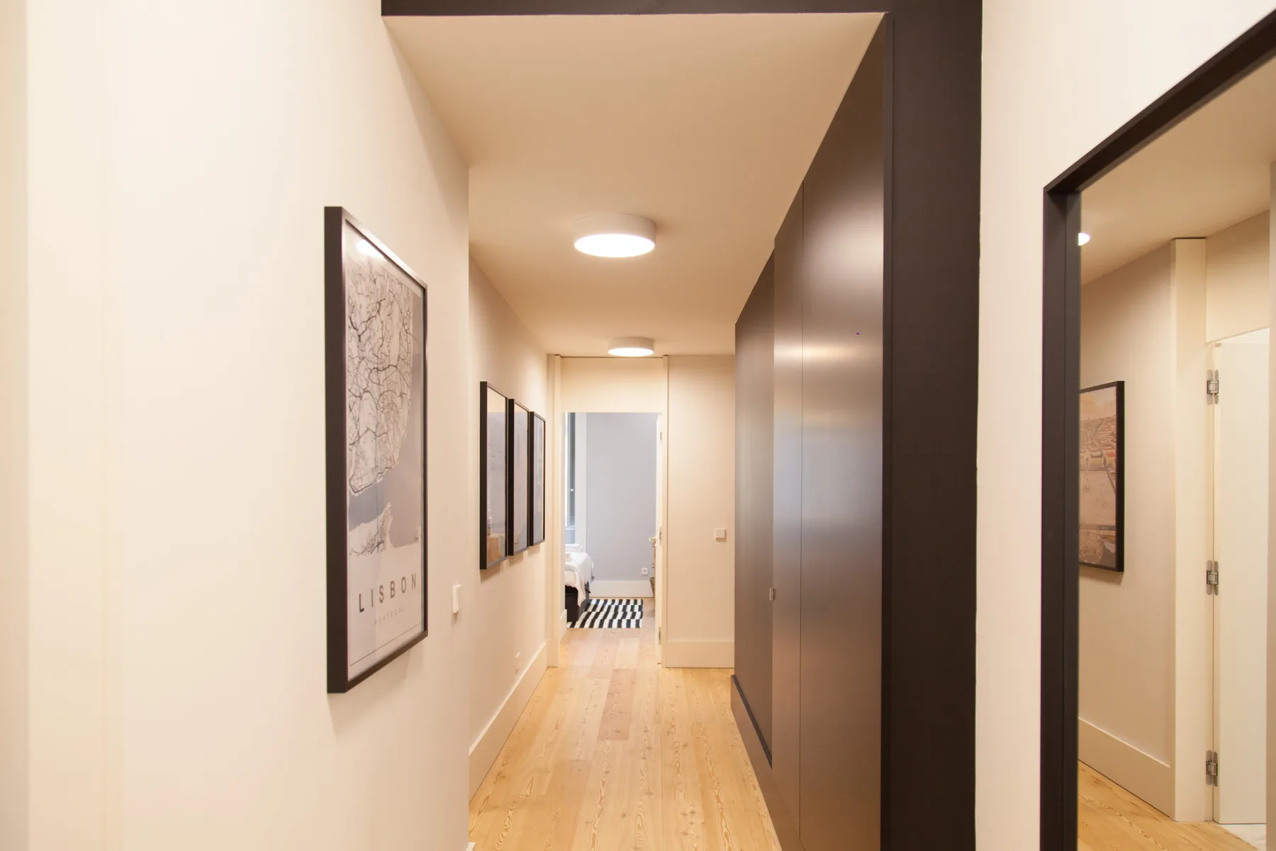A narrow interior hallway with framed artwork and light wood flooring.