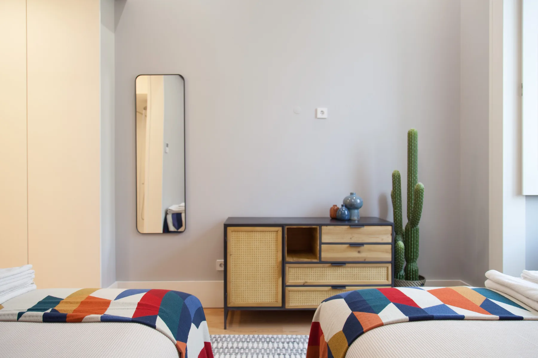 A bedroom with two beds, a low cabinet, and a tall cactus.