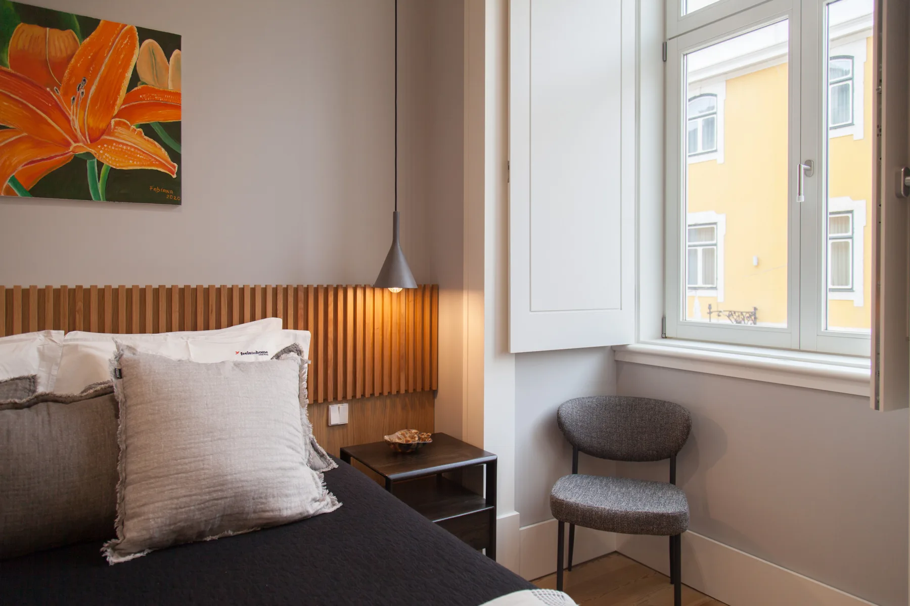 A bedroom with a bed, colorful floral artwork, and a window.