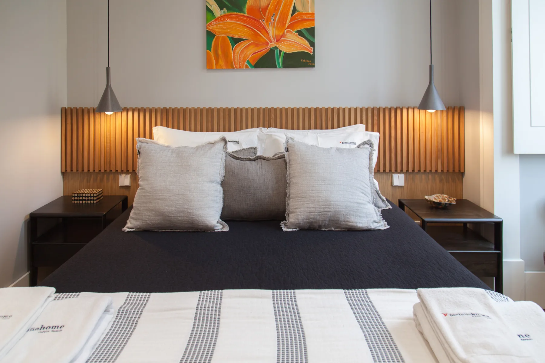 A bedroom with a neatly made bed, striped linens, and floral artwork above the headboard.