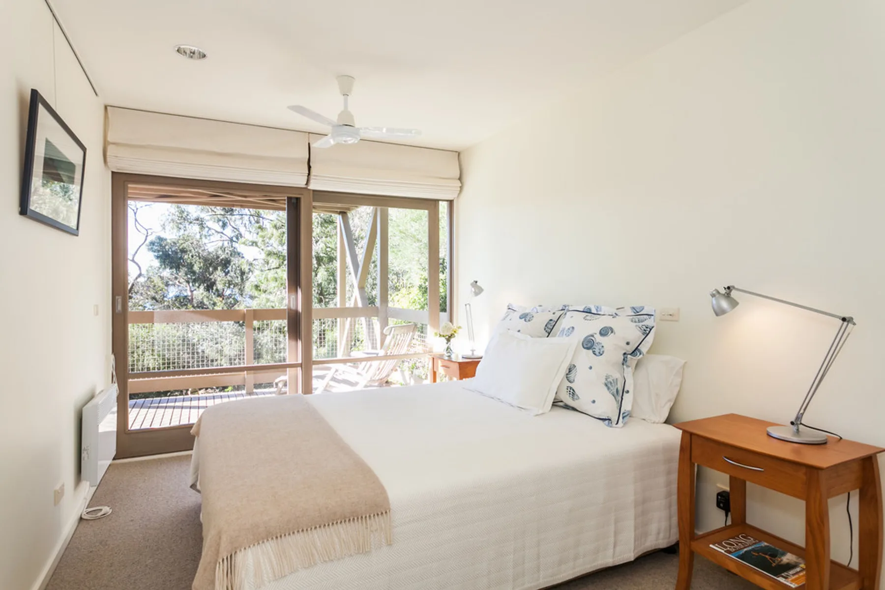 Un dormitorio luminoso con una cama junto a grandes ventanas con vistas a los árboles.