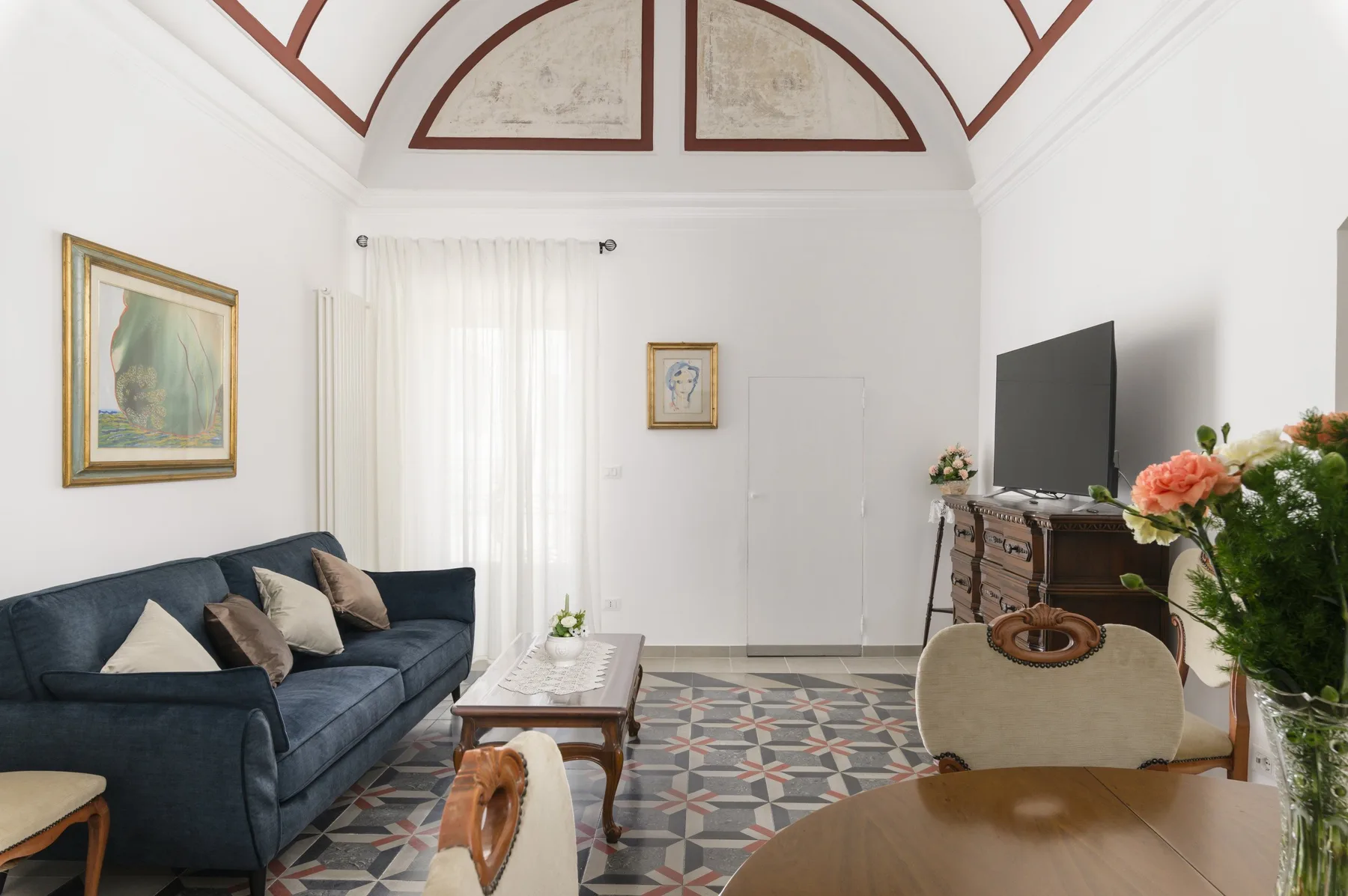 A bright living room with seating, a television, and patterned floor tiles.