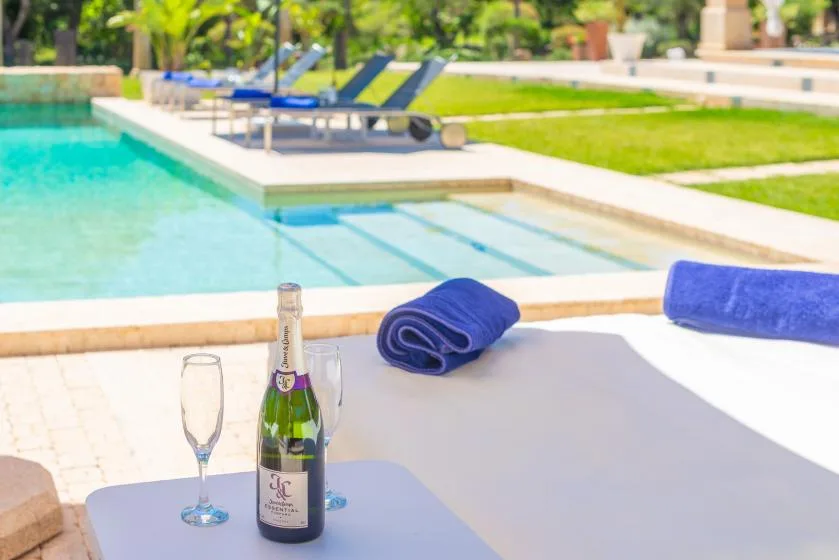 Una piscina junto a tumbonas, con una botella y copas sobre una mesa.