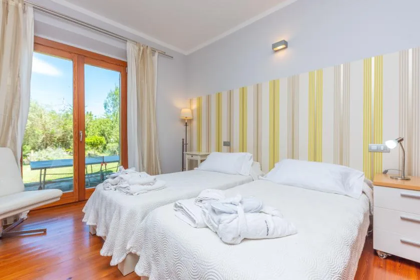 Un dormitorio luminoso con ropa de cama blanca y puertas de vidrio hacia un jardín.