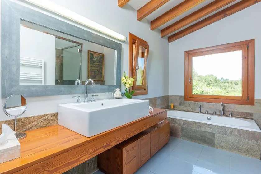 Un baño con lavabo, espejo amplio y bañera bajo una ventana.