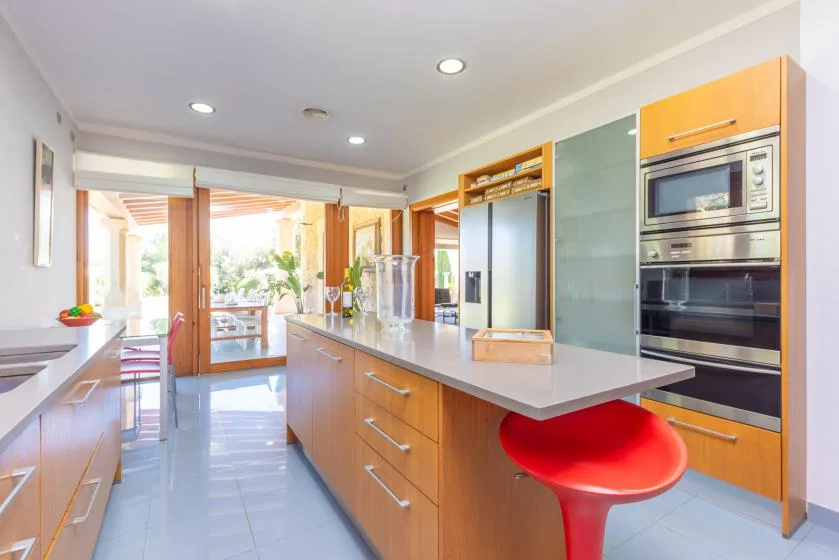 Una cocina luminosa con una isla larga y un asiento rojo de barra.