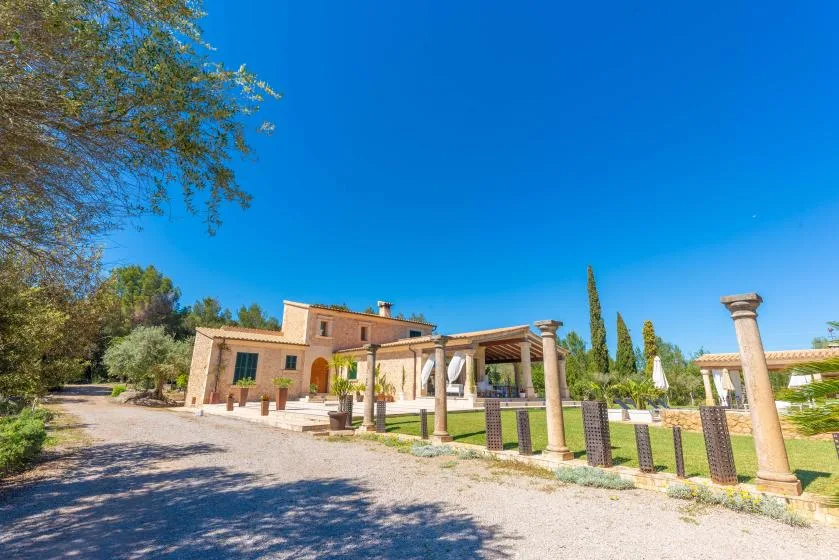 Una casa de ladrillo se encuentra junto a un camino de grava y una pérgola con columnas.