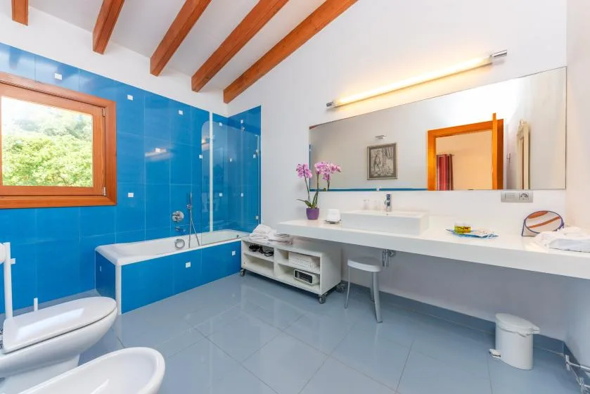 Un baño luminoso con azulejos azules, una bañera y una larga encimera con lavabo.
