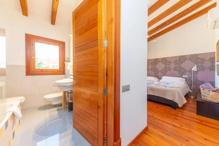 Se ven un baño y un dormitorio a través de una puerta de madera abierta.