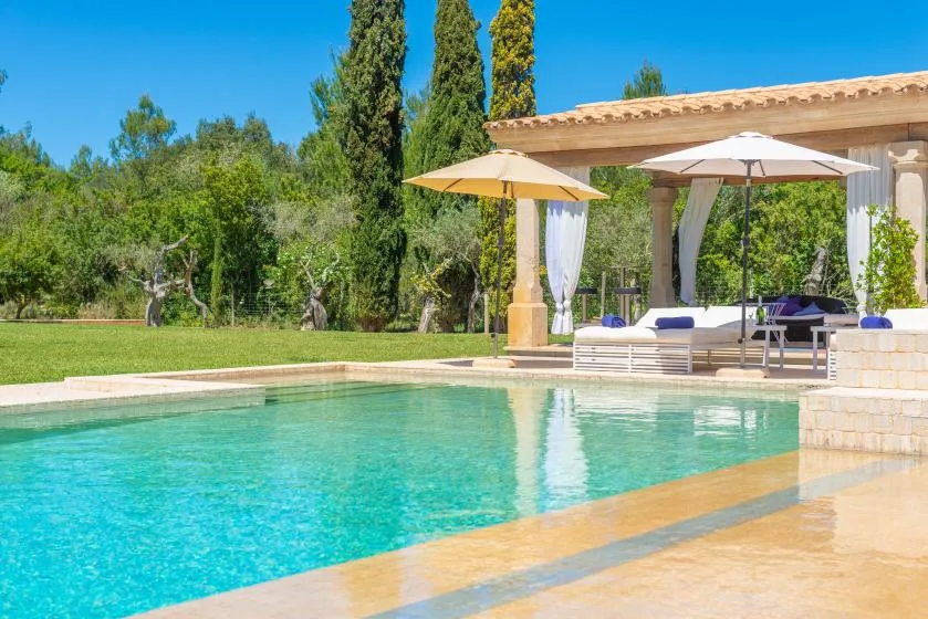 Una piscina al aire libre junto a un patio cubierto con asientos y sombrillas.