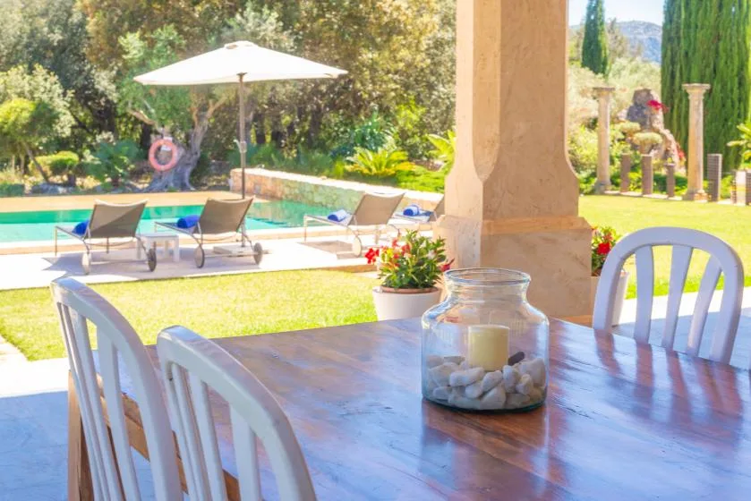 Una zona de comedor exterior a la sombra da a una piscina y un jardín.