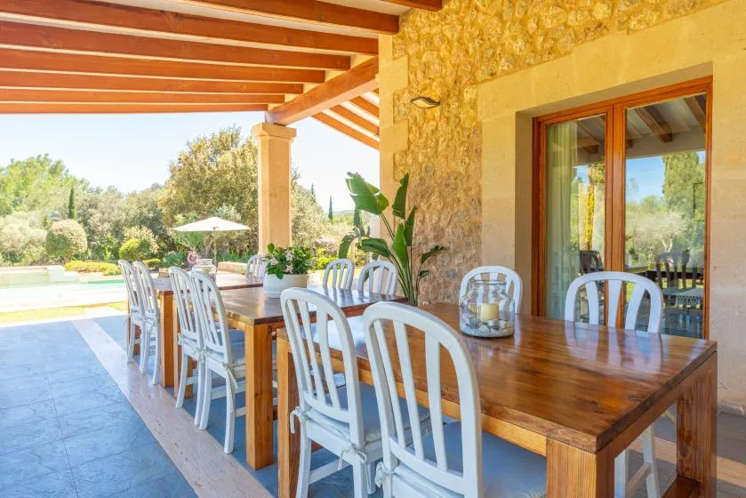 Comedor exterior cubierto con una mesa de madera y sillas blancas.