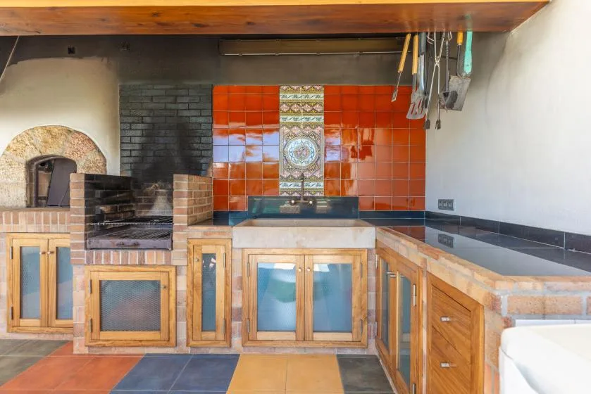 Una cocina exterior alicatada con zonas de cocción de ladrillo y armarios de madera.