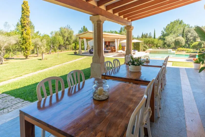 Una zona de comedor exterior cubierta da a un jardín y una piscina.