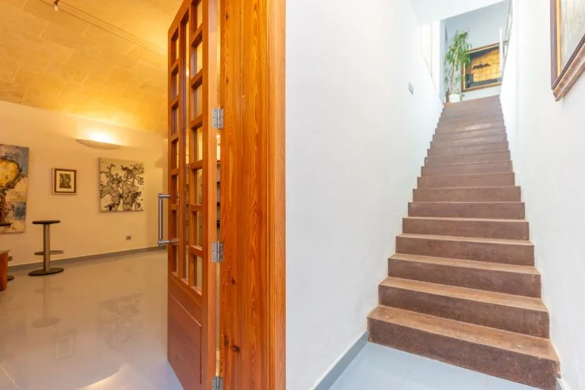 Una escalera interior sube junto a una puerta de madera abierta.