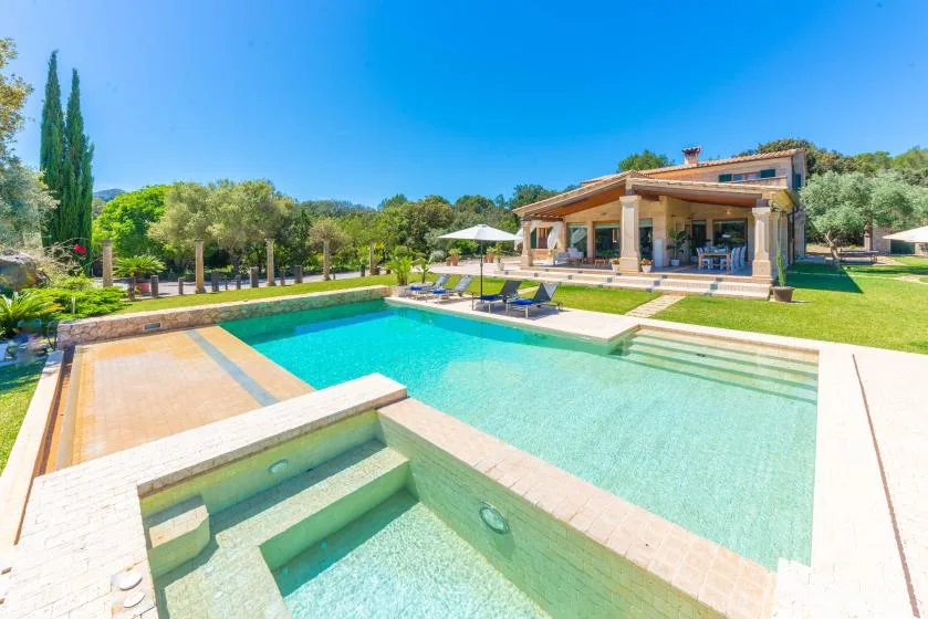 Piscina exterior junto a una casa moderna, con tumbonas sobre el césped.