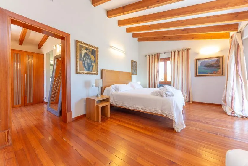 Un dormitorio luminoso con una cama, vigas de madera en el techo y suelo de madera.