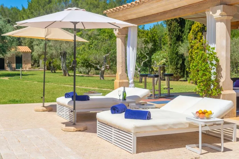 Un patio al aire libre con tumbonas acolchadas, sombrillas y vistas al jardín.