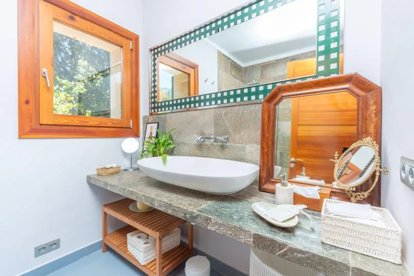 Un lavabo de baño con un espejo amplio, un lavamanos y una ventana con marco de madera.