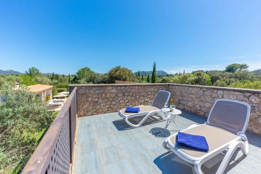 Una terraza en la azotea con tumbonas da a un paisaje verde bajo un cielo despejado.