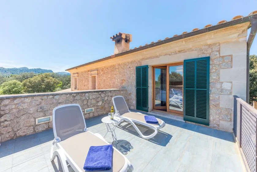 Una terraza soleada con asientos reclinables junto a una puerta abierta.